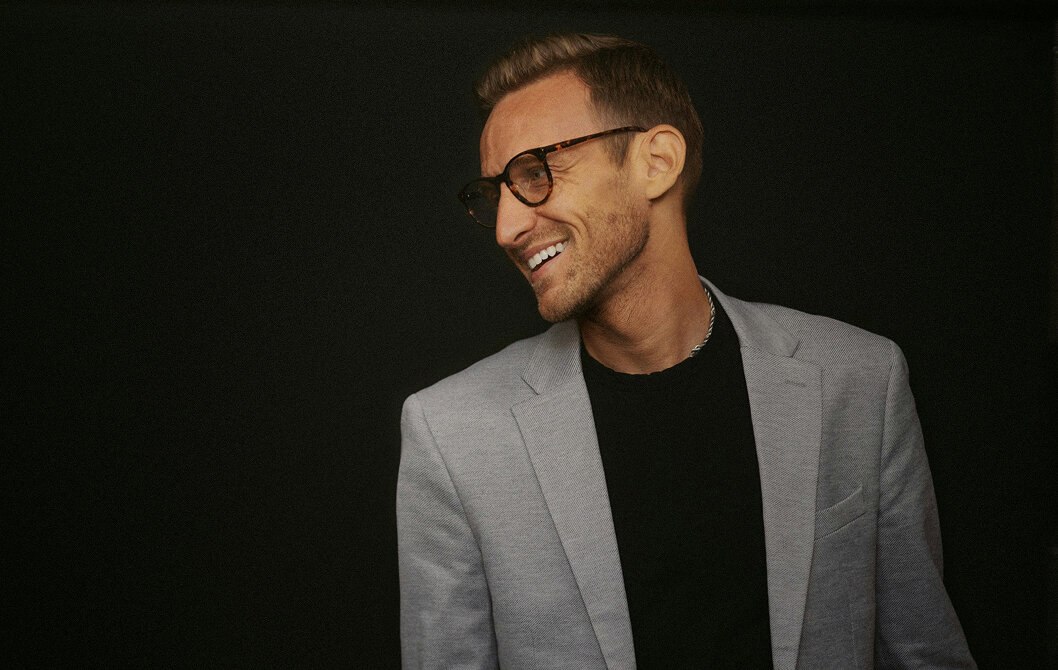 Mężczyzna w okularach i marynarce uśmiecha się.