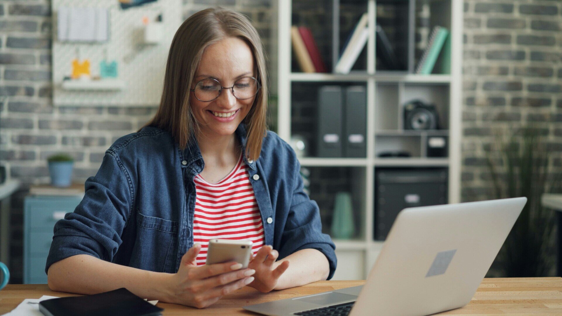 Osoba z telefonem i laptopem przy biurku.